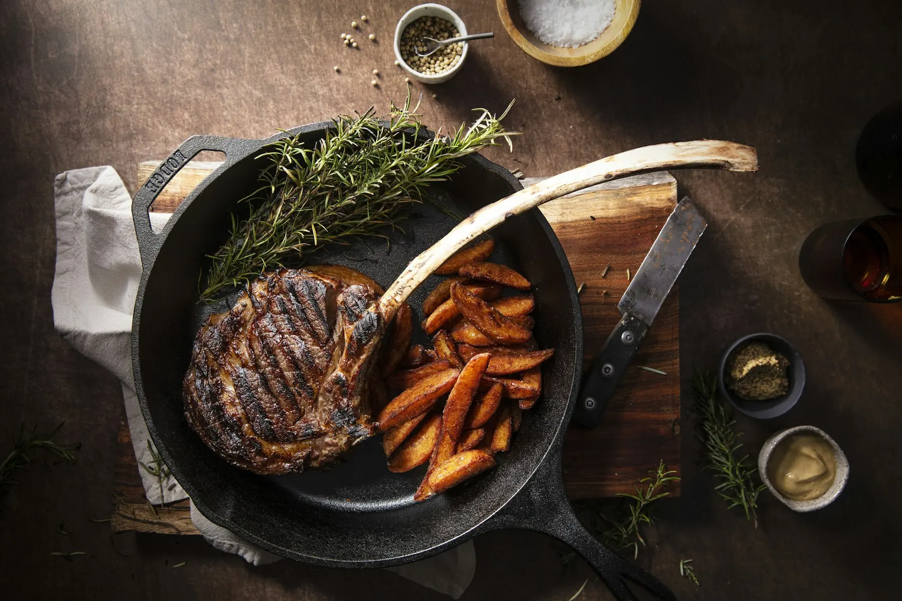 A thick ribeye seared in a cast iron skillet with fries and rosemary